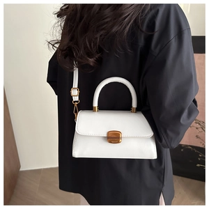 Detailed view of white leather handbag with golden metal clasp and round handle worn on shoulder