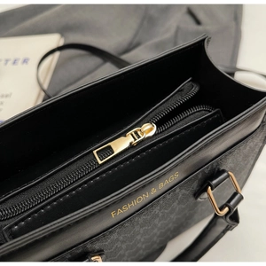 Nahaufnahme des goldenen Reißverschlusses und der Logo-Prägung auf der schwarzen Handtasche