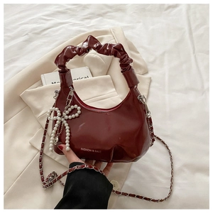 Detail of burgundy crescent bag with pleated handle and pearl bow charm on white fabric
