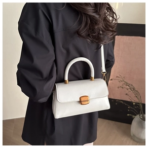 Detail view of cream structured handbag with lychee texture and gold square lock clasp