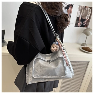 Close-up of metallic silver tote bag featuring a clear PVC window and plush charm accessory