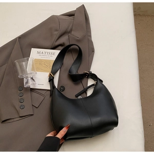 Detail of black leather crescent shoulder bag with gold hardware on white fabric background