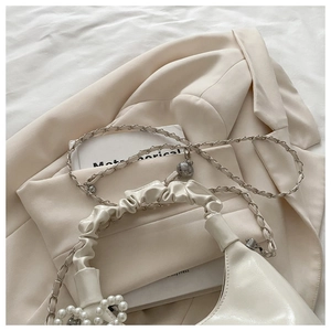 Detail of creamy white pleated handbag featuring a pearl bow and adjustable chain strap