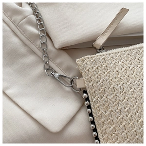 Detail einer beige gewebten Stroh-Clutch mit silbernen Nieten und einer Metallkette