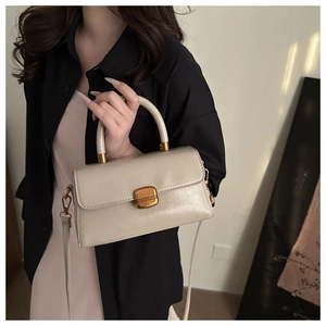 Detail of a vintage-style cream leather crossbody bag featuring a chunky gold metal buckle