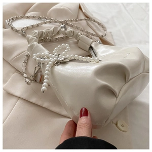 Detailed close-up of cream pleated handbag featuring a large pearl bow and chain strap