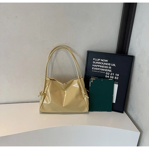 Close-up of a pale yellow patent leather tote bag featuring a knotted handle detail