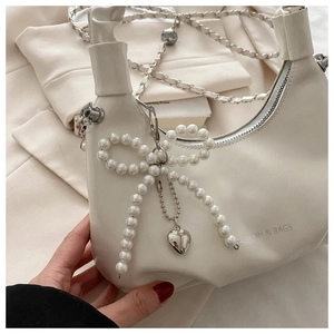 Detail of white pleated bag with pearl bow pendant and silver heart charm