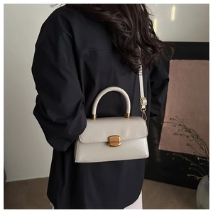 Detail of grey crossbody bag with round handle, gold clasp and adjustable strap on model