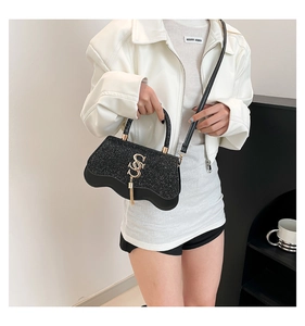 Detail of black glitter crossbody bag featuring gold SS logo and wavy edge design