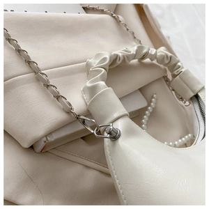 Detail of white half-moon bag featuring a pleated handle and silver metal chain strap