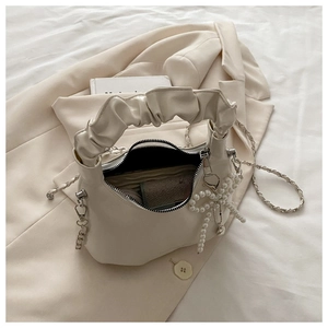Detail of cream pleated crossbody bag showing pearl bow charm and silver chain strap