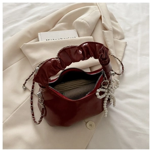Detail of burgundy pleated handbag featuring metallic chain strap and pearl bow charm