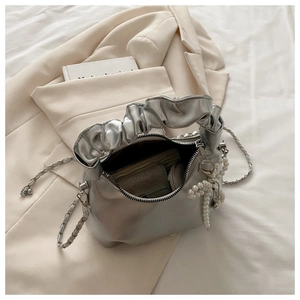 Close-up of silver chain strap and pearl bow charm on a pleated crossbody bag