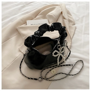 Close-up of black pleated cloud handle handbag with pearl bow charm on a beige blazer