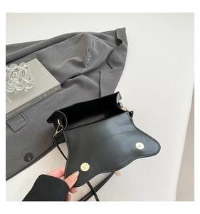 Detail view of the black leather crossbody bag featuring dual magnetic gold clasps