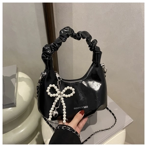 Detail of black patent leather crescent bag with pearl bow and ruffled handle
