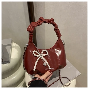 Detail of dark red glossy patent leather handbag with pearl bow and silver heart pendant