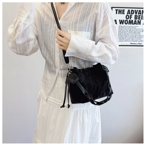 Detail of black pleated bucket bag with braided handle shown on a casual outfit