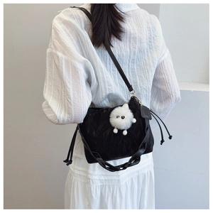Detail of black pleated bucket bag with braided strap and white plush monster charm