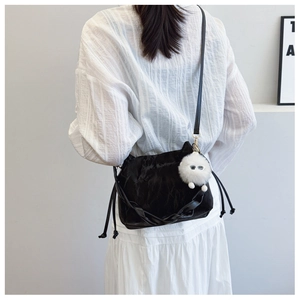 Detail of black glossy bucket bag with cute white plush monster pendant and drawstring