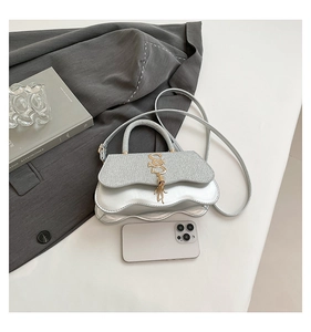 Detail of silver crossbody bag featuring a wavy edge, glitter flap, and golden S tassel buckle
