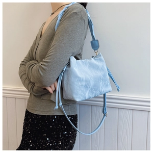 Detail of light blue bucket bag showing marble texture and woven shoulder strap