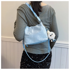 Detail view of light blue pleated cloud bag with a white plush doll charm and strap