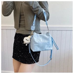 Detail of light blue bucket bag featuring ruffled texture, woven handle and plush charm