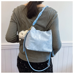 Detail of light blue bucket bag with pleated texture and fuzzy white pom-pom charm