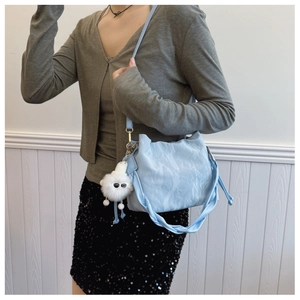 Light blue bucket bag with pleated texture and fuzzy pom-pom charm on simple background