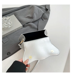Detail of silver crossbody bag featuring wavy flap design and dual magnetic closures
