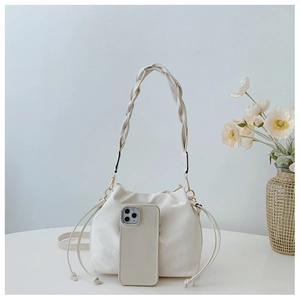 Detailed view of creamy white drawstring bucket bag with woven handle and phone for scale