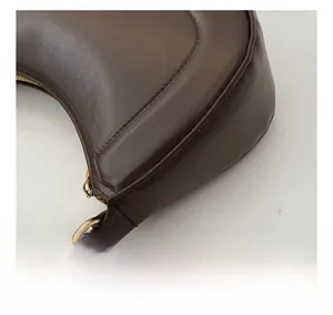 Detail of dark brown leather crescent bag showing stitching and golden hardware hooks