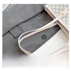 Detail of leather handles and gold metal rivets on a white monogram tote bag