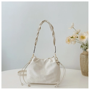 Macro detail of cream bucket bag with braided shoulder strap and gold hardware