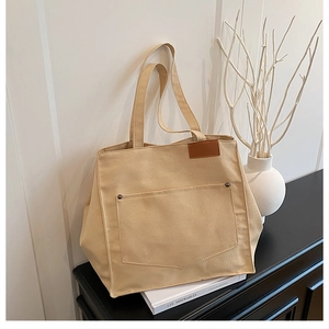 Détail du sac cabas en toile beige avec rivets métalliques et étiquette en cuir marron
