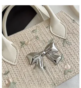 Detail of beige woven tote bag featuring green floral embroidery and silver metal bow