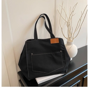 Détail d'un cabas en toile noire avec surpiqûres contrastées et étiquette en cuir en intérieur