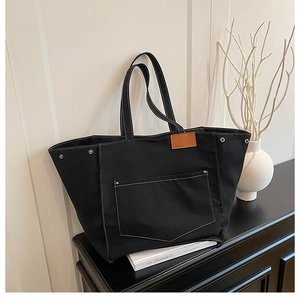 Détail du sac cabas en toile noire avec surpiqûres, rivets métalliques et garniture cuir