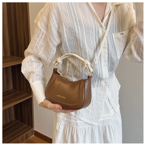 Detail of a brown leather semicircular bag featuring a white knotted handle and gold hardware