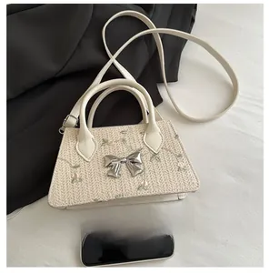 Mini straw handbag with floral embroidery and silver bow clasp shown next to a smartphone