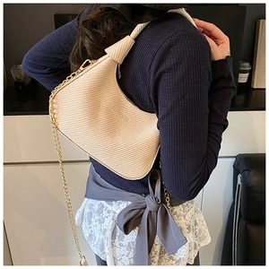 Detailansicht einer cremefarbenen gewebten Hobo-Tasche mit goldener Kette am Modell