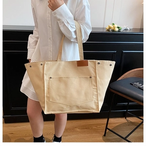 Détail d'un grand sac cabas en toile crème avec rivets métalliques et empiècement cuir