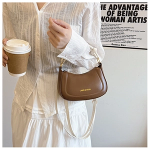 Detail of a brown half-moon saddle bag with white strap and gold logo lettering