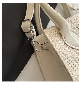 Detail of silver hardware hooks and adjustable strap on a floral straw shoulder bag