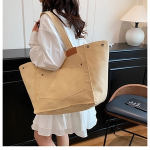 Détail d'un grand sac cabas en toile beige avec poche avant et finitions cuir