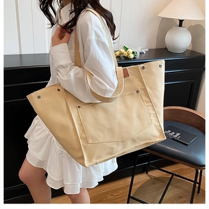 Détail du sac cabas en toile beige montrant l'étiquette en cuir, rivets et poche externe