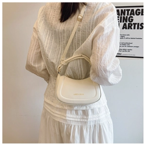 Detailed view of cream hobo bag with gold logo on white pleated skirt outfit background