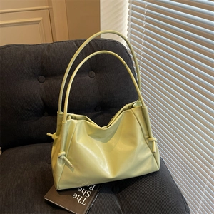 Light green faux leather tote bag with drawstring detail on a cozy blue velvet chair